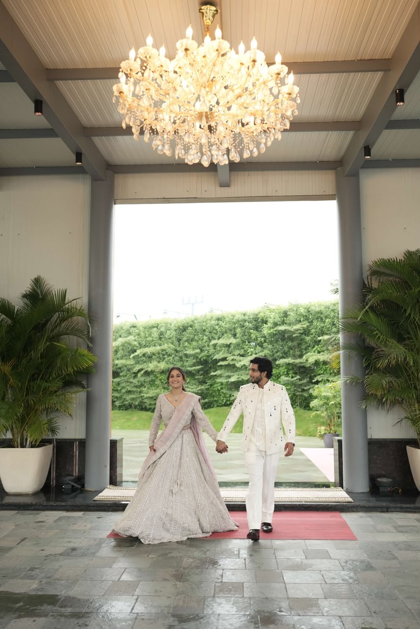 Shanya and Sparsh walking hand in hand under a chandelier
